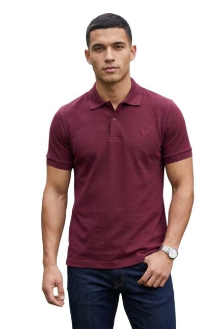 A man standing against a white background wearing a slim-fit, textured burgundy short-sleeve polo shirt with dark blue jeans and a silver watch.