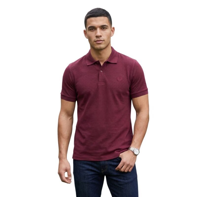 A man standing against a white background wearing a slim-fit, textured burgundy short-sleeve polo shirt with dark blue jeans and a silver watch.